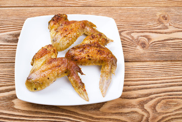 Baked chicken wings on a square plate on a wooden background 