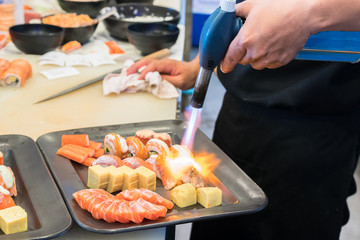 Torch burner over sushi rolls. Man's hand holding torch burner. Chef prepares uramaki sushi.
