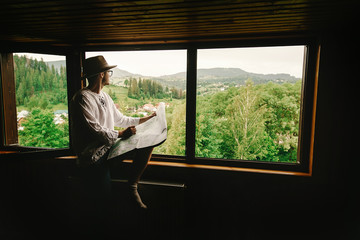 stylish hipster man sitting at window with view on mountains and