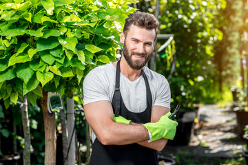 Portrait of handsome gardener in black apron and working gloves in the greenhouse.