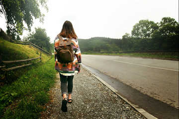 woman traveler with backpack walking down the road in mountains,
