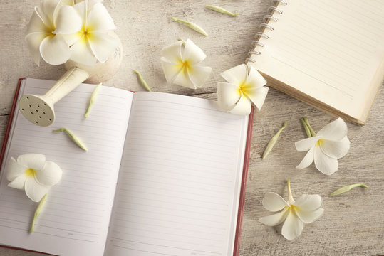 white plumeria flower and notebook on wood background in vintage tone 