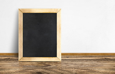 Empty Blackboard leaning at rustic wooden floor and white wall,