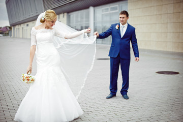 Bride in elegant dress raises her veil up standing behind a groo