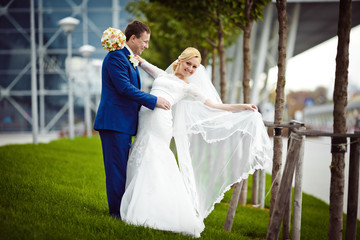 Bride smiles spreading her veil while standing in groom's hugs