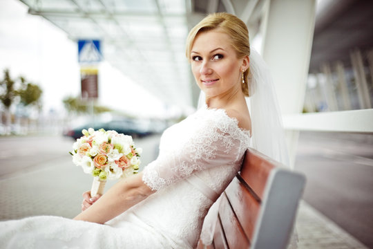 Pretty Bride Waits For Groom Sitting On The Bench At The Busstop