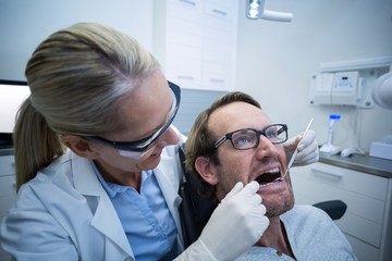 Female dentist examining male patient with tools 