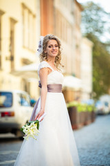 Naklejka premium Bride in dress with violet bow and a bouquet of callas poses on