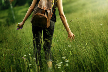woman traveler walking among grass in meadow and holding in hand