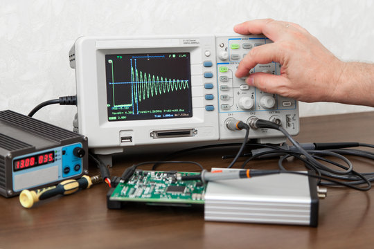 The man's hand turning signal adjustment knob on the oscilloscope panel