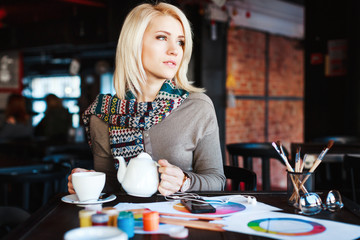 Girl sitting in cafe with cup of tea and drawings