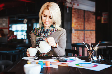 Girl sitting in cafe with cup of tea and drawings