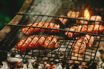 delicious grilled sausages roasting on grates with flames and sm