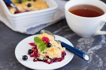 Berries crumble on a white plate and cup of tea on dark background. Pie with black currant and raspberry. 