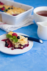Berries crumble on a white plate and cup of tea on blue  background. Pie with black currant and raspberry. 