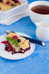 Berries crumble on a white plate and cup of tea on blue background. Pie with black currant and raspberry. 