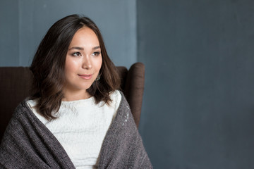 Obraz premium Beautiful woman in the room wrapped in a plaid blanket sitting in armchair dreaming and planning her autumn vacation