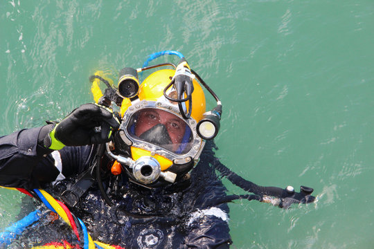 diver in the water in a diving suit and helmet ready to dive and showing sign ok