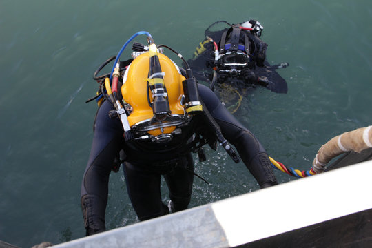 Photo of a diver in suit and helmet, which descends from the ship down to the water