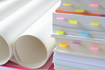 Pile of business documents with stick notes and roll of white papers on desk at workplace,high key tone.