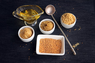 Set of different kinds of mustard - mustard seeds, mustard powder, french mustard, cremogenized and mustard oil - on black table.