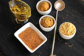 Set of different kinds of mustard - mustard seeds, mustard powder, french mustard, cremogenized and mustard oil - on black table.