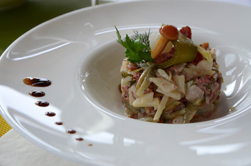 Tasty salad with meat, mushrooms, potatoes, cucumber and mayonnaise  on the background of the tablecloth
