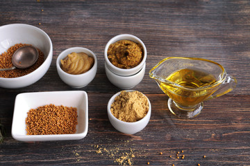 Set of different kinds of mustard - mustard seeds, mustard powder, french mustard, cremogenized and mustard oil - on wooden table.
