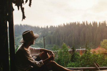 hipster man sitting on porch of wooden house  looking at woods i