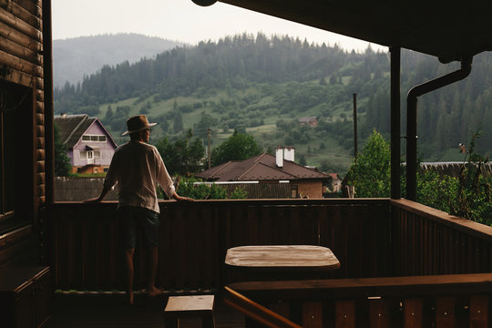 Hipster Man Standing On Porch Of Wooden House And Relaxing Looki