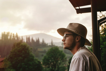 hipster man on porch of wooden house  looking at mountains in ev