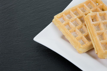 Zwei Waffeln serviert auf eckigem weissen Teller. Auf einer Schieferplatte stehend im Anschnitt.
