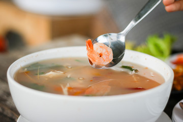 woman use spoon scoop shrimps from Sour prawn soup or Tom Yum Ku