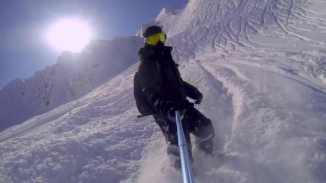 Man riding on snowboard with selfie stick in his hand