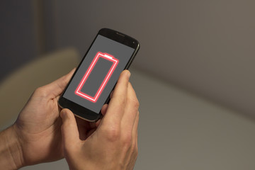 Hands holding mobile phone with low battery on the screen.