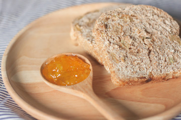 whole wheat bread and orange jam are on the wooden plate
