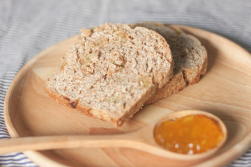whole wheat bread and orange jam are on the wooden plate