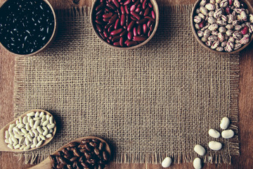 Beautiful multi-colored beans in bowls and wooden spoons on a background of burlap