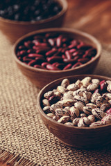 Beautiful multi-colored beans in ceramic bowls on a background of burlap