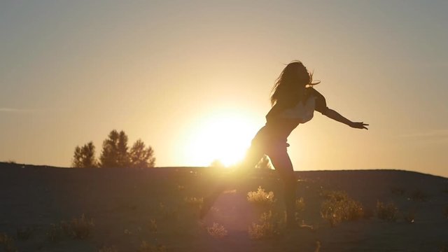silhouette of a girl a professional dancer jumping at sunset in the desert