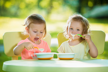 Two little girls sitting at a table and eating together against green lawn