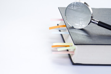 Textbook with multicolor bookmarks and magnifying glass