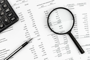 Magnifying glass, pen and calculator on financial business paper.