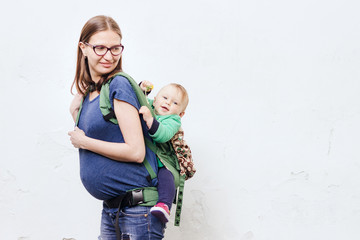 Pregnant young woman with her little son in baby carrier