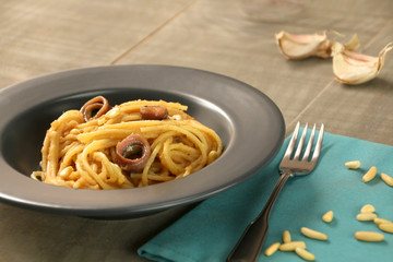 A grey dish of spaghetti with breadcrumbs, anchovies, garlic and pine nuts. A fork and some pine...