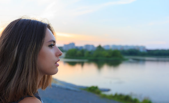 Young Beautiful Woman Portrait Against Sunset In Park And City At Background