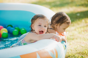 The two little baby girls playing with toys in inflatable pool in the summer sunny day