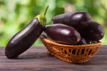 eggplant in a wicker basket on wooden table with blurred green background