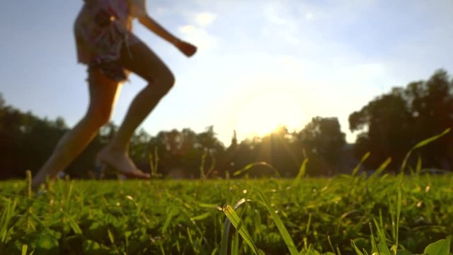 Super slow motion clip of attractive girl running barefoot on the grass holding her shoes in her hand