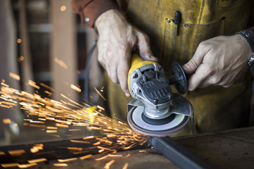 Custom furniture worker grinds weld seam on steel frame. - obrazy, fototapety, plakaty